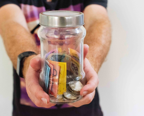 person holding glass jar filled with Australian money